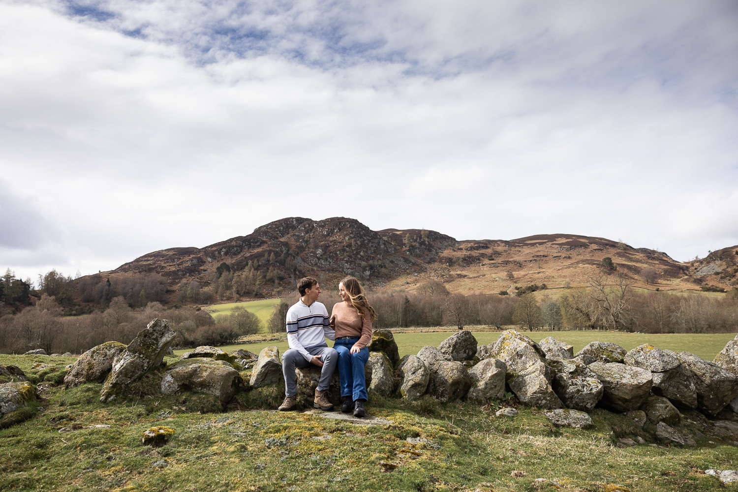 couple sitting on the rocks with mountains in the background